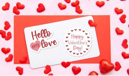 a red card with a "Hello my love" sticker and a "Happy Valentine's Day!" sticker, surrounded by red heart-shaped candies on a pink background.
