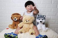 A young child sitting on a bed, surrounded by stuffed animals, including a teddy bear, a lion, and a husky.