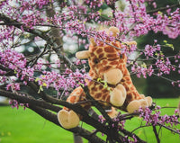 A stuffed giraffe toy is perched on a tree branch, surrounded by blooming pink flowers.