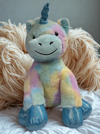 A plush toy of a unicorn with a blue horn and glittery feet is sitting on a white surface.