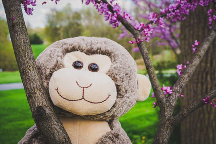 A stuffed monkey toy is sitting on a tree branch, surrounded by blooming purple flowers.
