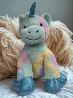 A plush toy of a unicorn with a blue horn and glittery feet is sitting on a white surface.