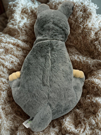A plush gray stuffed animal, possibly a bear or a similar creature, is lying on a soft, textured surface, such as a blanket or a bed.