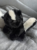 A black and white stuffed animal toy, resembling a skunk or a similar animal, is sitting on a gray blanket.