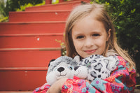 A young girl with blonde hair is smiling and holding a stuffed animal, with a red staircase in the background.