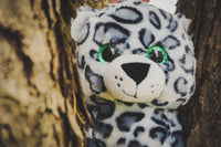 A stuffed toy leopard with large green eyes peeking out from behind a tree trunk.