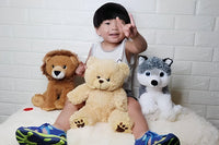 A young child sitting on a bed, surrounded by stuffed animals, including a brown lion, a yellow teddy bear, and a gray husky.