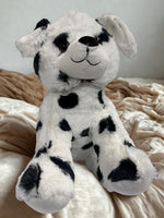 A stuffed dalmation dog toy is sitting on a bed with a beige blanket.