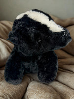 A black and white stuffed animal toy is sitting on a beige blanket.
