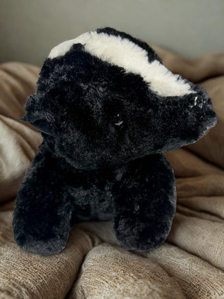 A black and white stuffed animal toy is sitting on a beige blanket.