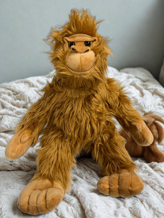 A plush toy of an orangutan sitting on a bed with a white blanket.
