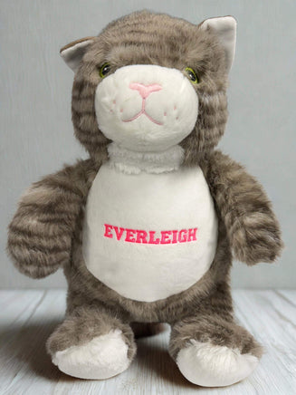 A stuffed cat toy with a white belly and gray fur, sitting on a wooden surface.