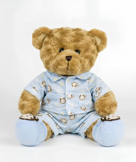 A brown teddy bear wearing a blue pajama outfit with monkey designs sits on a white background.