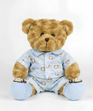 A brown teddy bear wearing a blue pajama outfit with monkey designs sits on a white background.