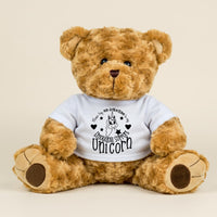 A brown teddy bear wearing a white t-shirt with a graphic design and text printed on it.