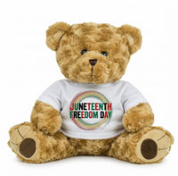 A brown teddy bear wearing a white t-shirt with the text "JUNEEENTH FREEDOM DAY" printed on it.