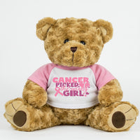 A brown teddy bear wearing a pink shirt with the text "Cancer Picked Me" printed on it.