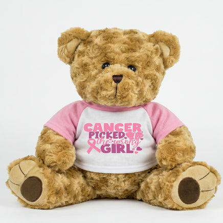 A brown teddy bear wearing a pink shirt with the text "Cancer Picked Me" printed on it.