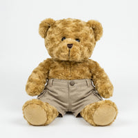A brown teddy bear wearing khaki cargo shorts sits on a white background.