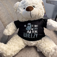 A white teddy bear wearing a black t-shirt with a cartoon character and text printed on it.