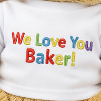 A white t-shirt with colorful embroidered text that says "We Love You Baker!"