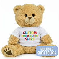 A brown teddy bear wearing a white shirt with colorful text on it.