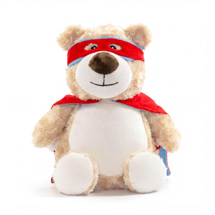 A stuffed teddy bear wearing a red cape and a red bandana, sitting on a white background.