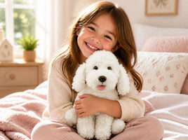Smiling girl on a cozy bed hugging a white poodle stuffed animal from the Baker's Bears 16 inch DIY plush kit