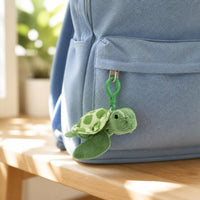 Sea turtle plush bag clip hanging from the zipper of a light blue backpack