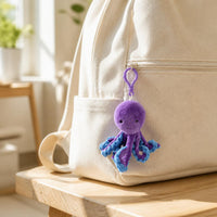 Octopus plush bag clip hanging from the zipper of a cream canvas backpack